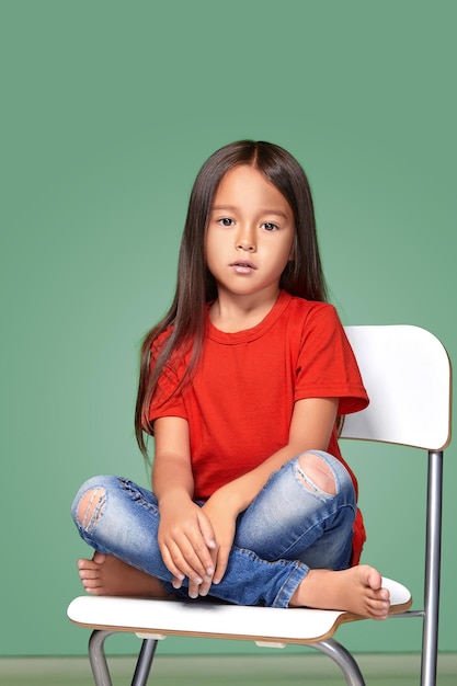 Foto gratuita niñita con camiseta roja y posando en una silla con fondo verde