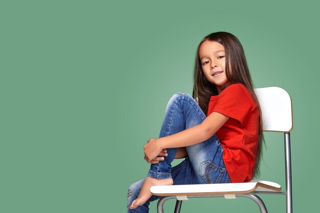 niñita con camiseta roja y posando en una silla con fondo verde