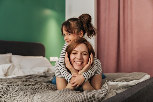 Niño abraza a mamá. Mujer y su hija se encuentran en la cama.