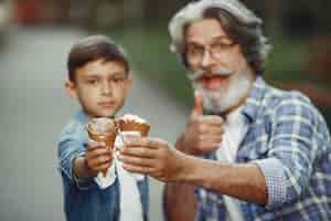 Foto gratuita niño y abuelo están caminando en el parque. anciano jugando con su nieto. familia con helado.