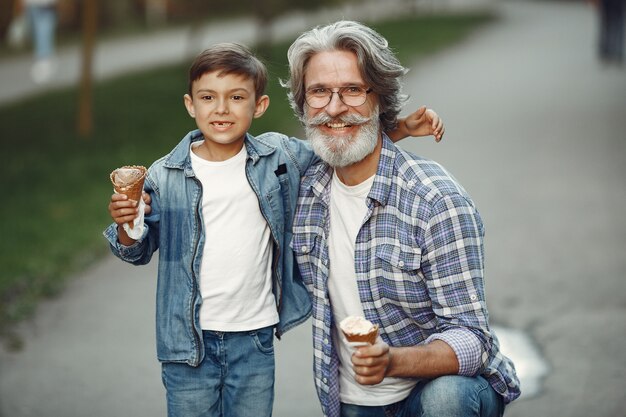 Niño y abuelo están caminando en el parque. Anciano jugando con su nieto. Familia con helado.