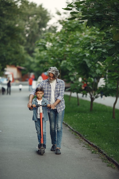 Niño y abuelo están caminando en el parque. Anciano jugando con su nieto. Niño con scooter.