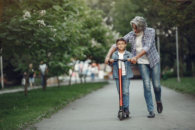 Niño y abuelo están caminando en el parque. Anciano jugando con su nieto. Niño con scooter.