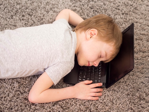 Foto gratuita niño acostado con la cabeza en una computadora portátil