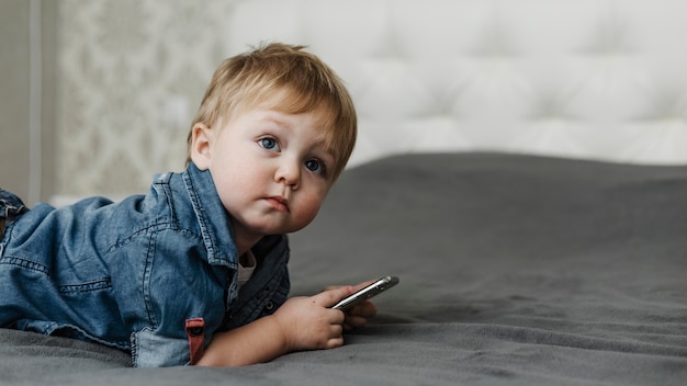 Foto gratuita niño acostado en la cama y sosteniendo el teléfono móvil