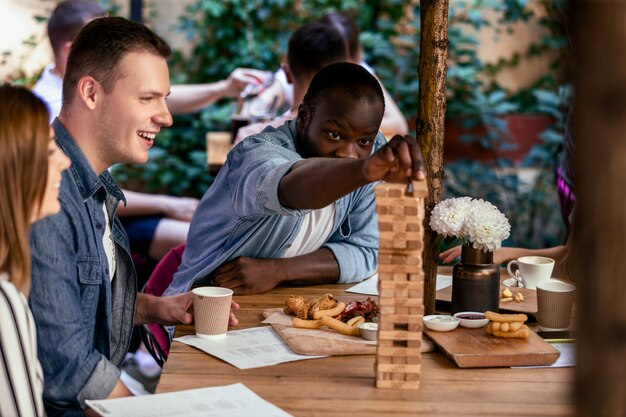 Niño africano está jugando jenga juego de mesa con mejores amigos caucásicos en el acogedor restaurante local