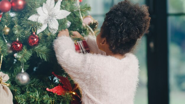 Niño afroamericano decorado con adornos en el árbol de Navidad