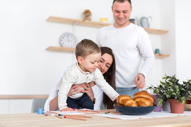 Niño agarrando cruasanes con sus padres en la cocina