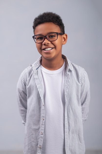 Niño alegre en elegantes espectáculos de pie contra el fondo blanco.