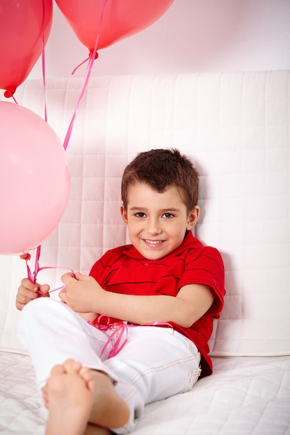 Foto gratuita niño alegre con globos sentado en el sofá