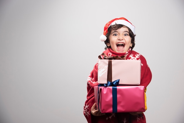 Niño alegre con gorro de Papá Noel con regalos de Navidad