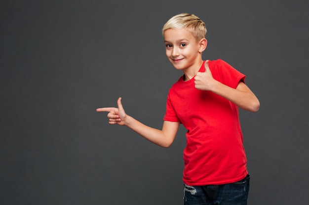 Niño alegre del niño pequeño que señala mostrando los pulgares para arriba.