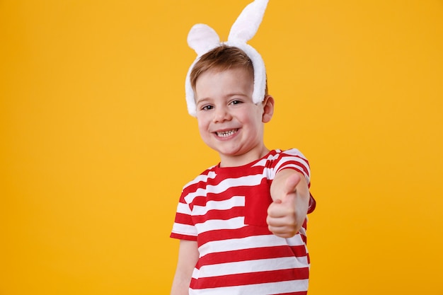 Niño alegre con orejas de conejo y mostrando los pulgares para arriba