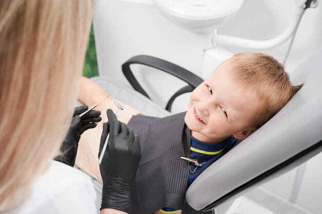 Niño alegre sentado en una silla dental en el consultorio dental