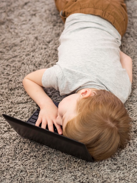 Niño de alto ángulo acostado con la cabeza en una computadora portátil