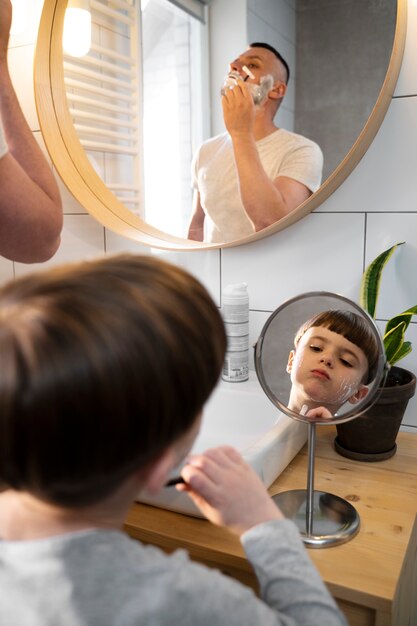 Niño de alto ángulo aprendiendo a afeitarse con espejo