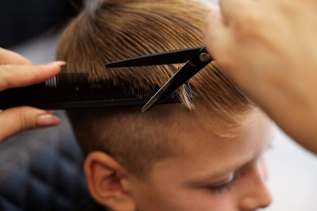 Niño de alto ángulo cortándose el pelo en el salón