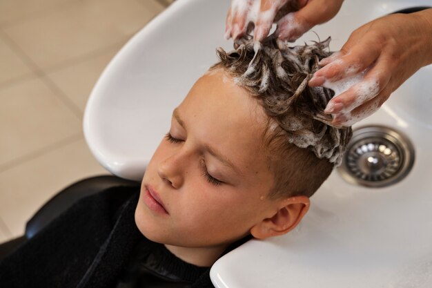 Niño de alto ángulo que se lava el cabello en el salón