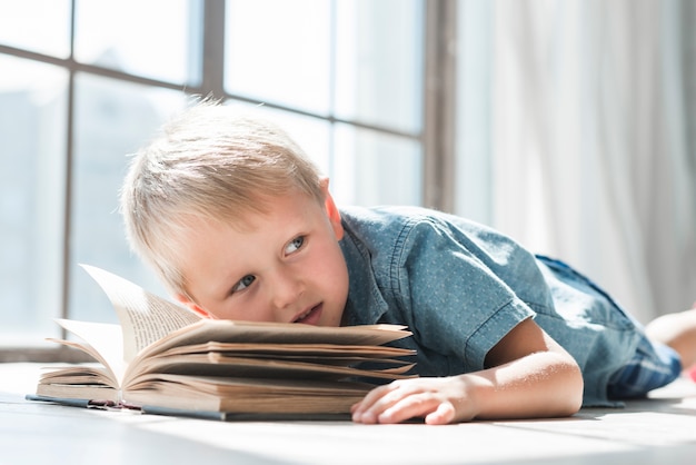 Niño apoyado en un libro abierto cerca de la ventana