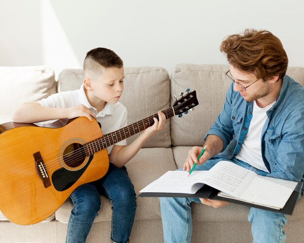 Niño aprendiendo guitarra y tutor escuchando