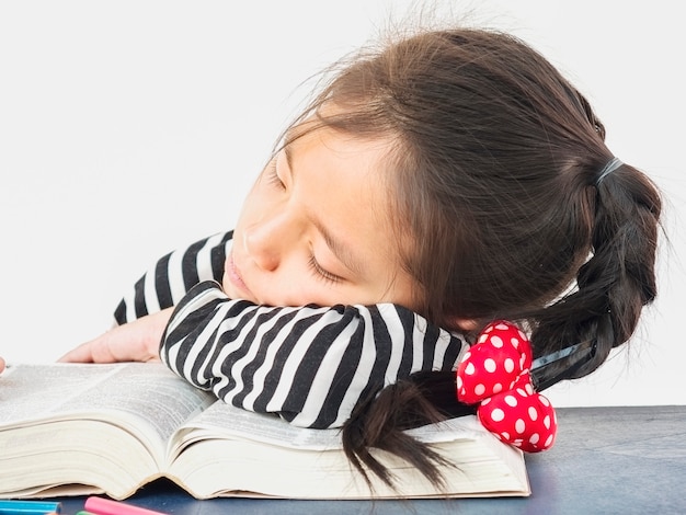 Un niño asiático duerme mientras lee un gran libro.