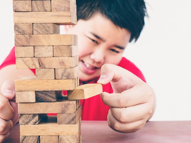 Un niño asiático está jugando al juego de la torre de bloques de madera para practicar habilidades físicas y mentales.