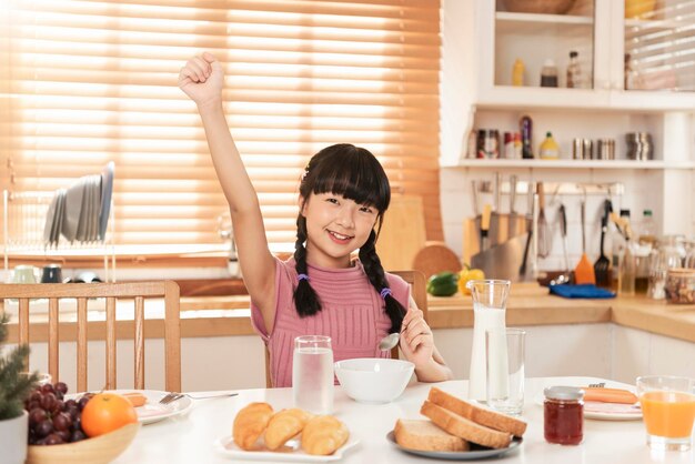 Niño asiático feliz comiendo cereal y desayuno con leche en la cocina en casa