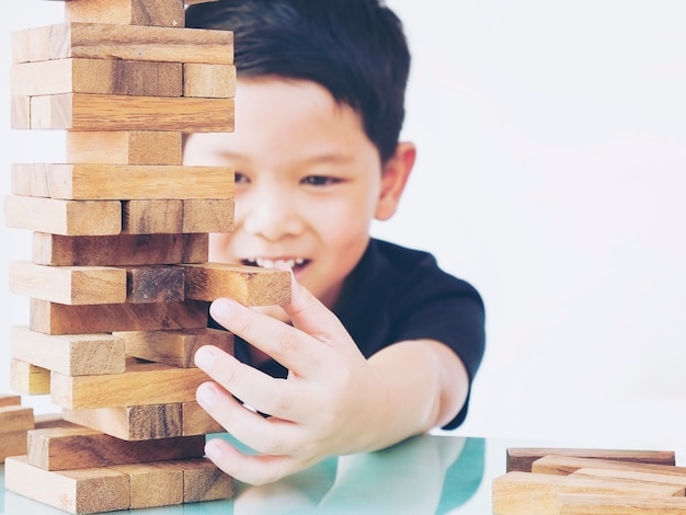 Foto gratuita un niño asiático está jugando al juego de la torre de bloques de madera para practicar habilidades físicas y mentales.