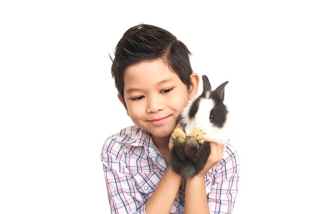 Niño asiático que juega con el conejo encantador del bebé aislado sobre blanco