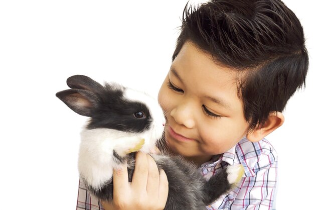 Niño asiático que juega con el conejo encantador del bebé aislado sobre blanco