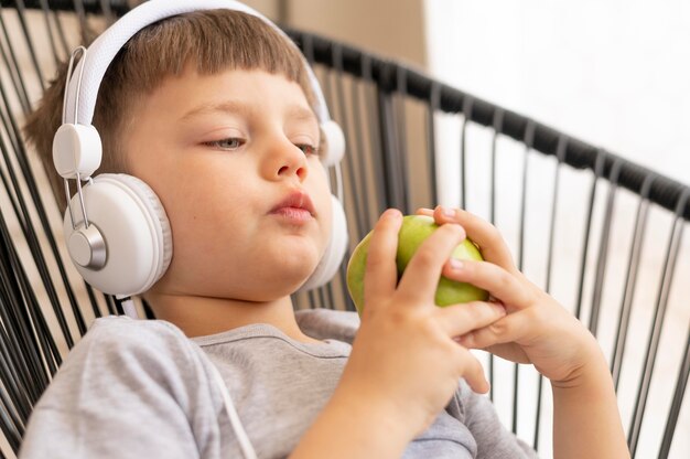 Niño con auriculares comiendo manzana