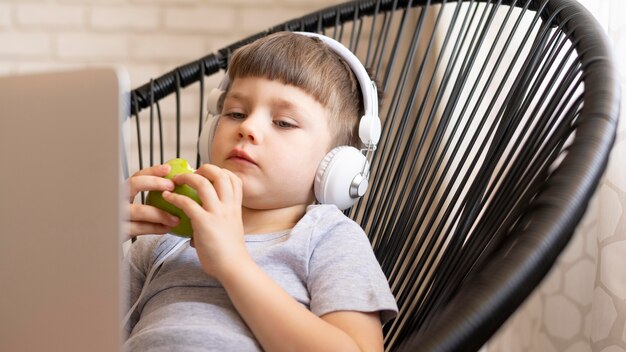 Niño con auriculares en silla comiendo manzana