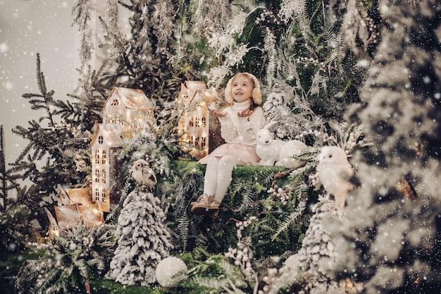 Foto gratuita niño bastante caucásico con cabello largo rubio sonríe y se sienta en un ambiente navideño con un conejito