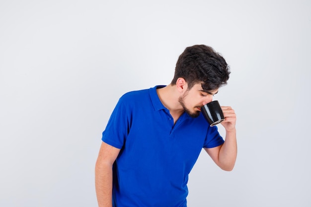 Niño bebiendo una taza de té en camiseta azul y mirando serio. vista frontal.