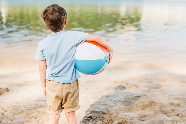 Foto gratuita niño con bola de viento mirando el agua