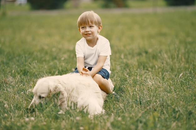 Niño con cabello rubio jugando en el césped con su perro. Niño vestido con camiseta blanca y pantalón azul