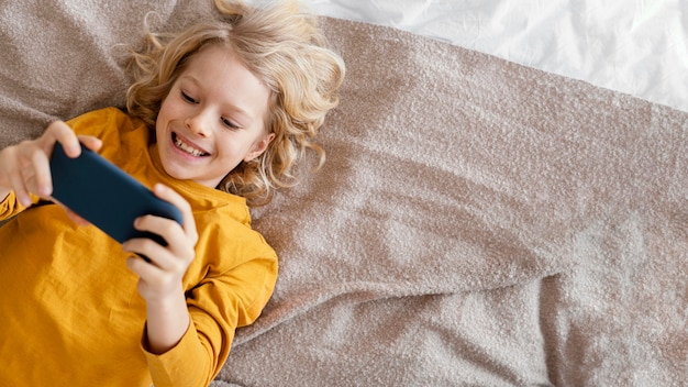 Foto gratuita niño en la cama jugando en el móvil