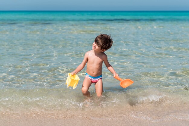 Niño caminando con juguetes en el agua en la playa