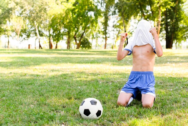 Niño sin camisa saliendo victorioso después de marcar un gol