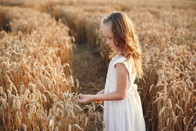 Niño en un campo de trigo de verano. Niña con un lindo vestido blanco.