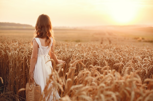 Niño en un campo de trigo de verano. Niña con un lindo vestido blanco.
