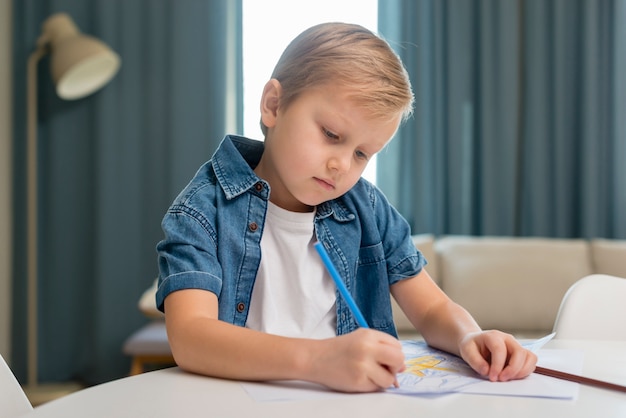 Foto gratuita niño en casa sentado a la mesa y escribe