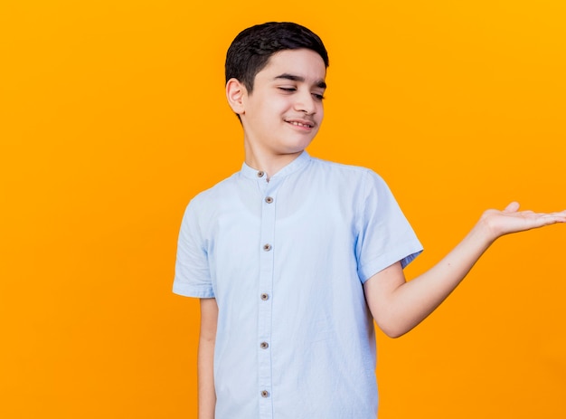 Niño caucásico joven disgustado mostrando la mano vacía mirándolo aislado sobre fondo naranja con espacio de copia