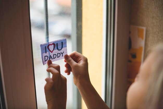 Niño colocando una nota en la ventana para su padre
