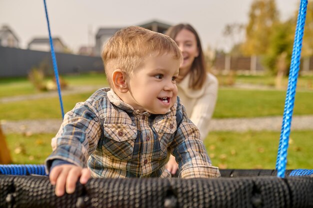 Niño en columpio mirando al lado y mujer detrás