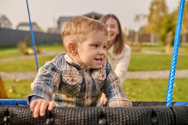 Niño en columpio mirando al lado y mujer detrás