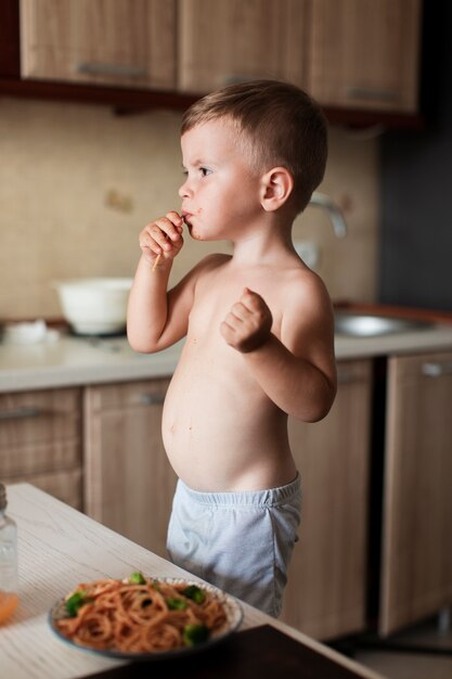 Niño comiendo espagueti en la cocina