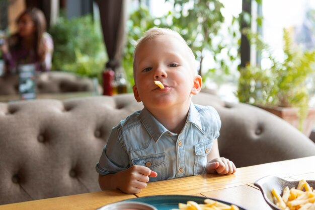 Niño comiendo papas fritas en el restaurante