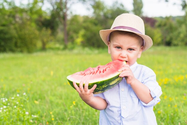 Niño comiendo rebanada de sandía en el parque