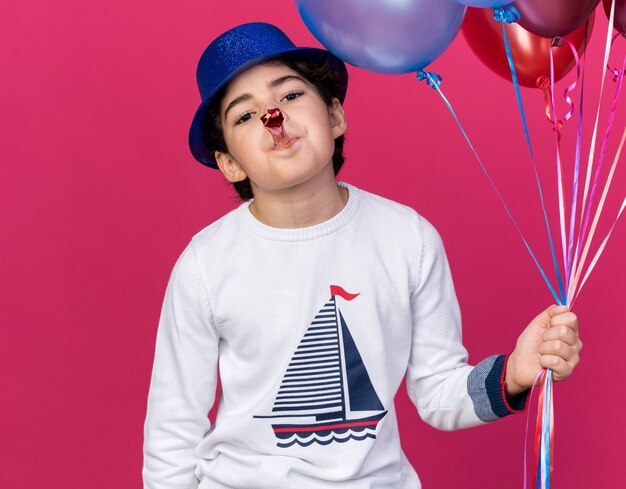 Foto gratuita niño contento con gorro de fiesta azul sosteniendo globos soplando silbato de fiesta